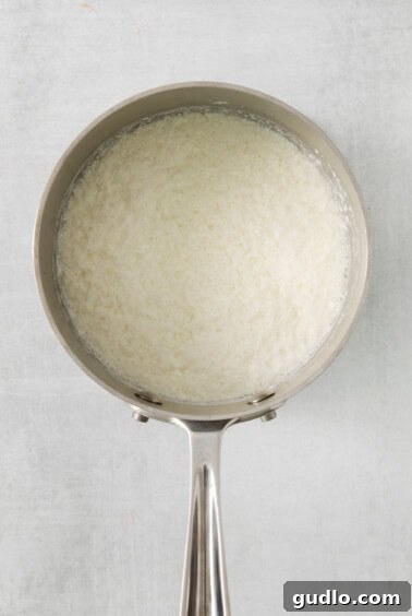 Milk gently simmering in a pan on a white background, demonstrating the initial step of bringing the milk to a soft boil for curdling.