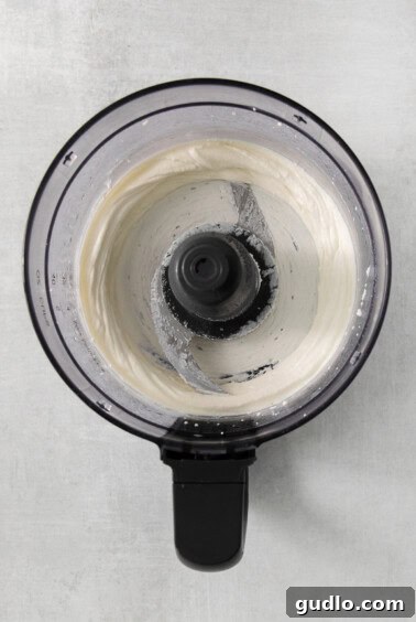 A food processor actively blending white cheese curds, demonstrating the transformation into smooth, creamy homemade cream cheese.