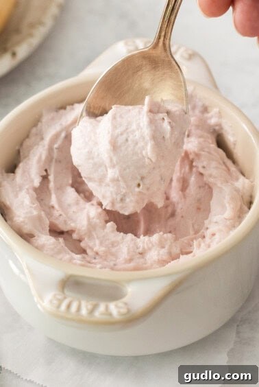 A person expertly scooping luscious strawberry whipped cream cheese into a pristine white bowl, highlighting the creamy texture and vibrant color of the homemade spread.