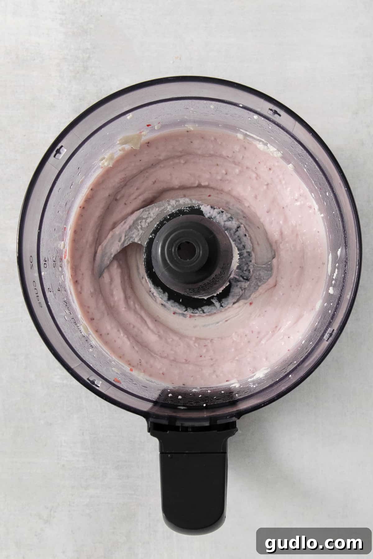 A food processor containing a swirling pink liquid, indicating the perfect blend of creamy cheese and strawberry puree.