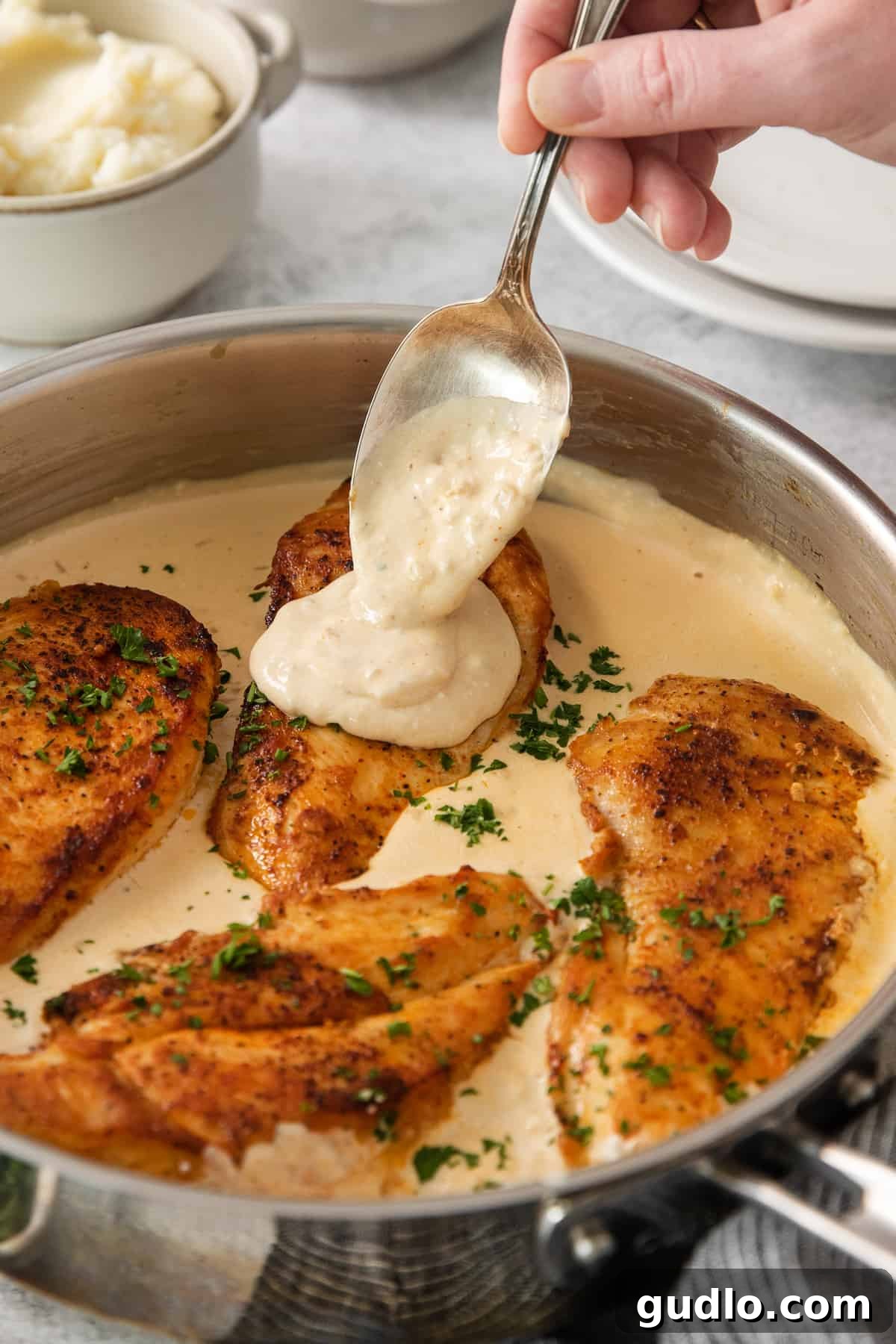 Crispy Garlic Chicken Delight 5 A person carefully pouring the rich, creamy garlic sauce over perfectly seared chicken breasts nestled in a hot skillet, ready to be served.