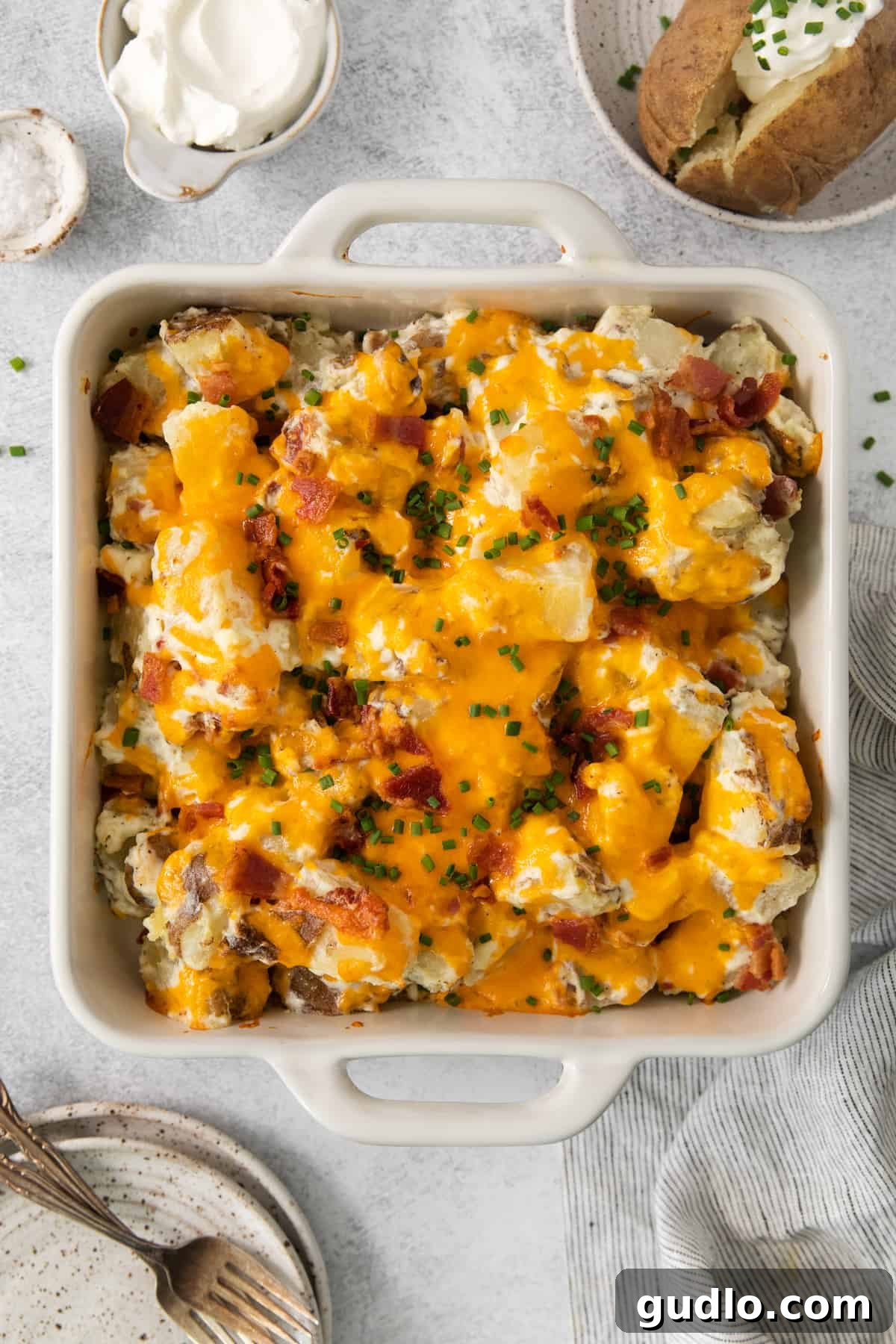 Ultimate Loaded Potato Bake 2 Cheesy potato casserole in a casserole dish, topped with golden cheese and crispy bacon.