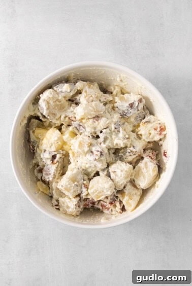 Ultimate Loaded Potato Bake 10 Creamy potato mixture in a white bowl on a grey background, after mashing with butter, cream cheese, and seasonings.