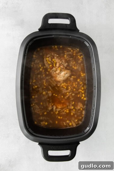 Shredded chicken being stirred back into the chili mixture in a slow cooker.