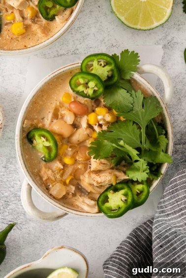 A finished bowl of creamy white chicken chili with garnishes like lime and jalapeños.