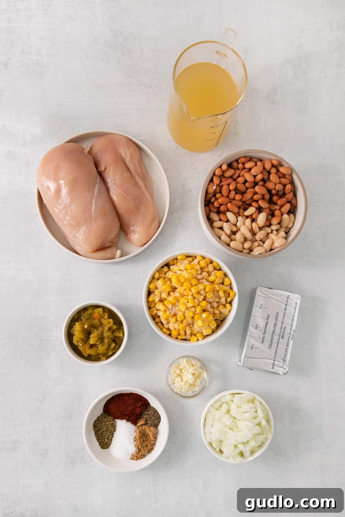 Creamy Slow Cooker White Chicken Chili 3 A vibrant display of fresh ingredients including chicken breasts, various beans, corn, onions, and spices, meticulously arranged on a rustic wooden table, ready for cooking.