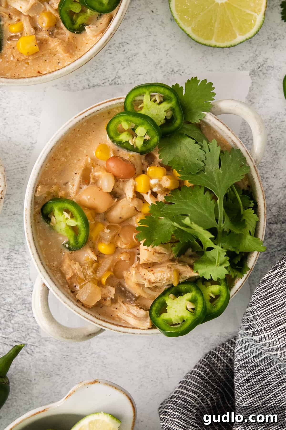 Creamy Slow Cooker White Chicken Chili 5 A beautifully presented bowl of white chicken chili, garnished with vibrant green cilantro and fresh lime slices, against a light background.