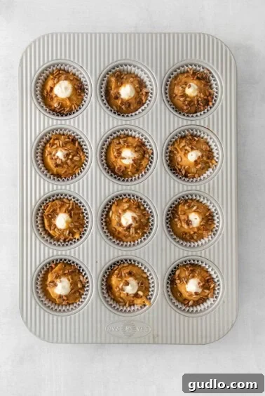 Cream Cheese Swirl Pumpkin Muffins 14 A muffin tin filled with unbaked chocolate cupcakes, generously topped with a crumbly praline or streusel mixture, ready for baking.