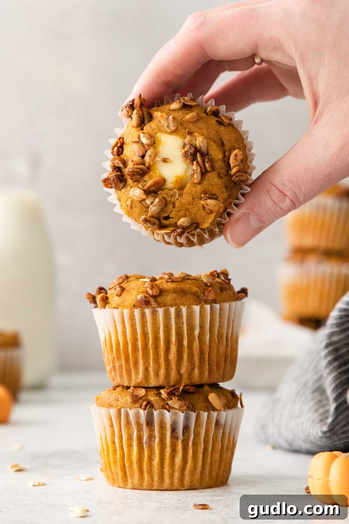 Cream Cheese Swirl Pumpkin Muffins 5 A hand reaching for a stack of freshly baked pumpkin muffins, highlighting their inviting appearance and soft texture.