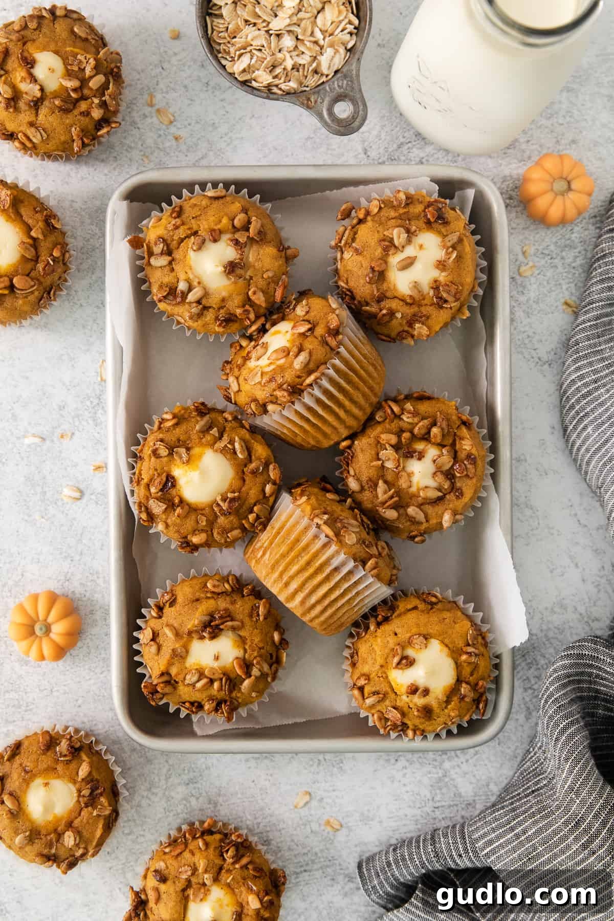 Cream Cheese Swirl Pumpkin Muffins 7 A charming still life featuring freshly baked pumpkin muffins on a wooden tray, accompanied by a glass of milk and scattered oats, evoking a cozy autumnal scene.