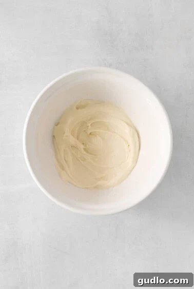 Cream Cheese Swirl Pumpkin Muffins 9 A bowl filled with smoothly whipped cream cheese filling on a pristine white surface, ready for piping.