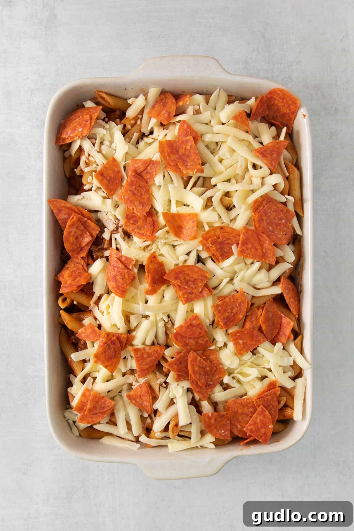 A bubbly and golden-brown pizza casserole in a white baking dish, fresh from the oven, topped with melted cheese and pepperoni.