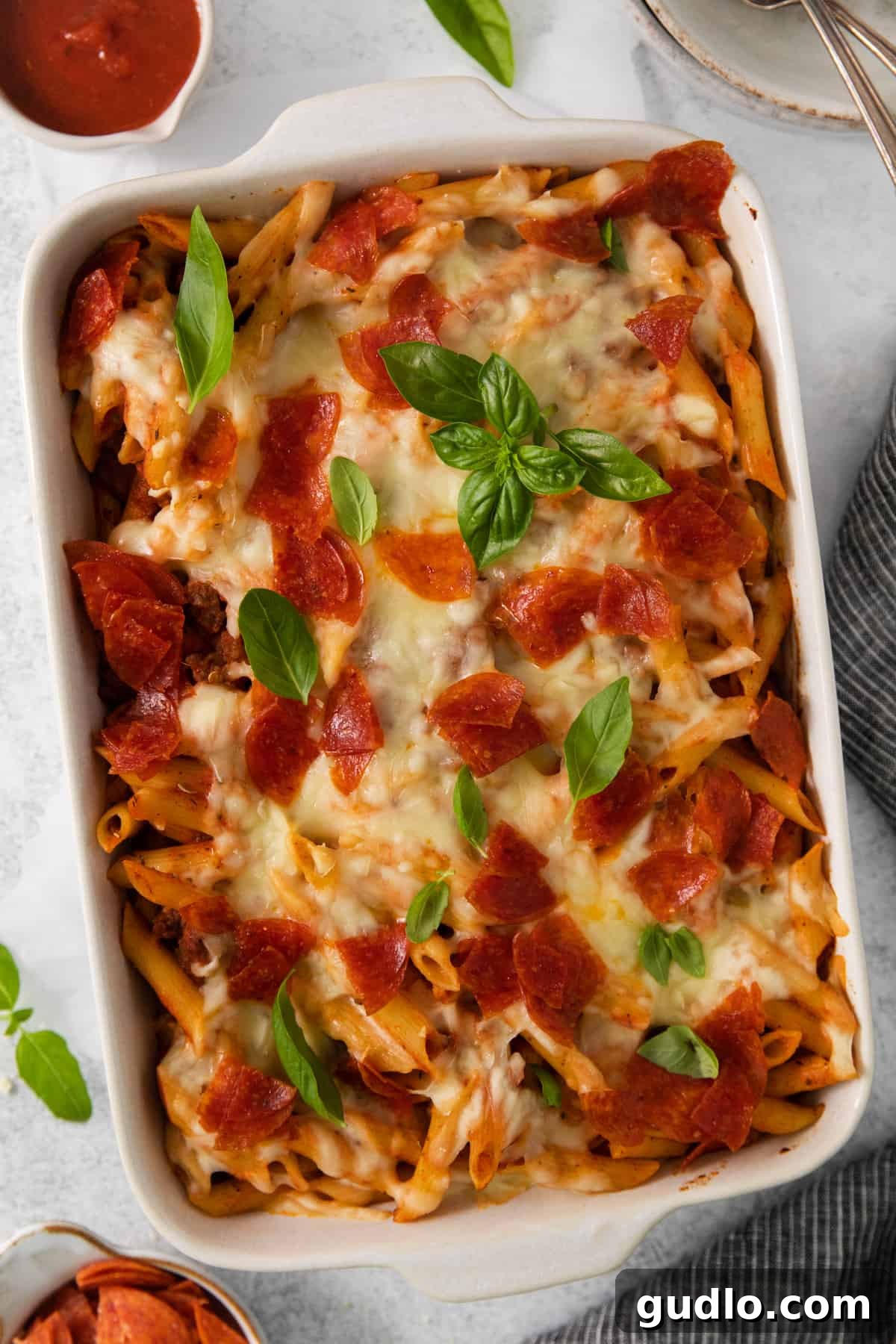 A close-up of a pepperoni and basil-garnished pasta dish, highlighting the rich sauce and textures.
