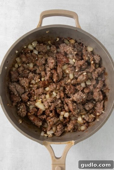 A skillet filled with browned ground Italian sausage and sautéed onions.