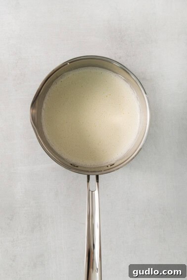 Decadent Banana Cream Cheese Pudding 9 A metal spoon stirring warm milk in a saucepan over low heat, showing the beginning of the pudding process.