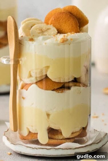 Decadent Banana Cream Cheese Pudding 13 A layered banana trifle in a glass, ready to be served, with a wooden spoon beside it.