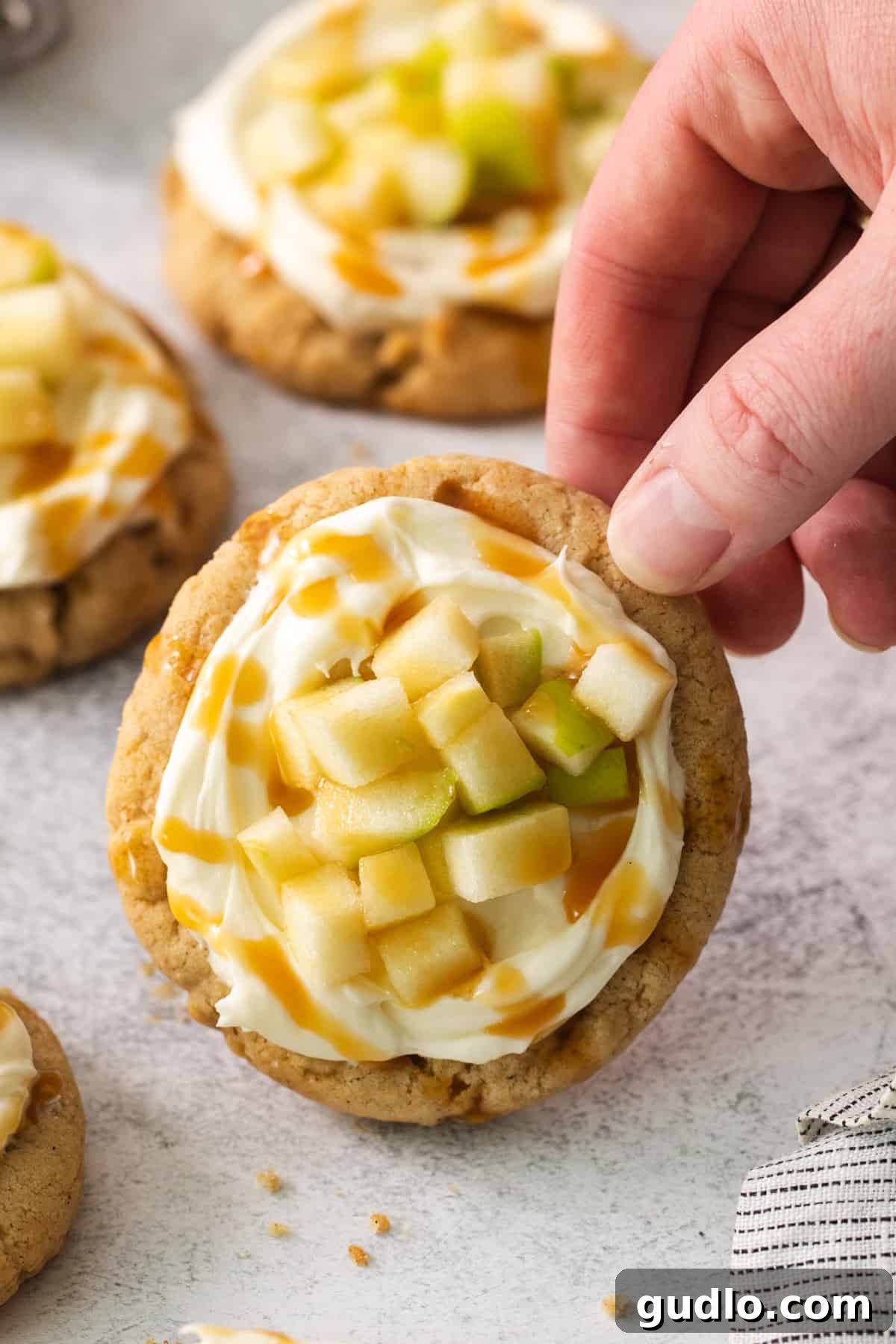 Caramel Apple Cheesecake Cookies 8 A hand reaching for a finished cream cheese caramel apple cookie, ready to be enjoyed.