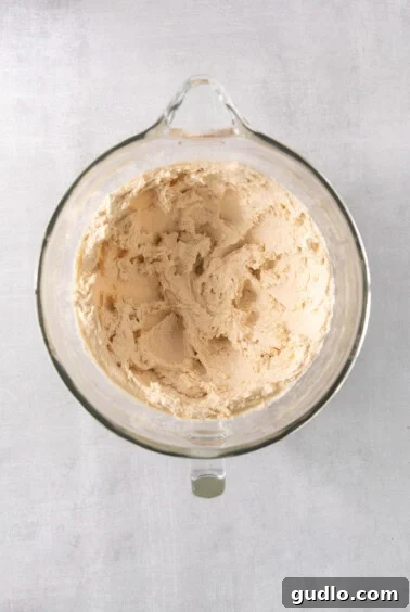 A glass bowl with creamed butter and sugars in a stand mixer, demonstrating the first step of cookie dough preparation.