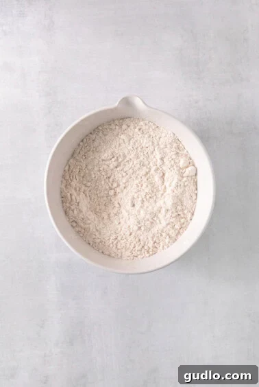 A white bowl filled with dry ingredients, showcasing the combined flour, spices, and leavening agents for the cookie dough.