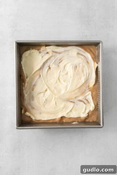 Swirled Apple Cream Cheese Coffee Cake 13 A pan filled with a smooth, white cream cheese frosting on top of the coffee cake batter.