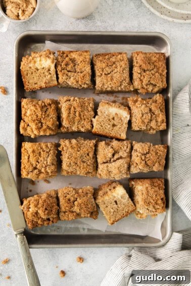 Swirled Apple Cream Cheese Coffee Cake 16 A pan filled with freshly baked Apple Cream Cheese Coffee Cake, already sliced, next to a cup of coffee.