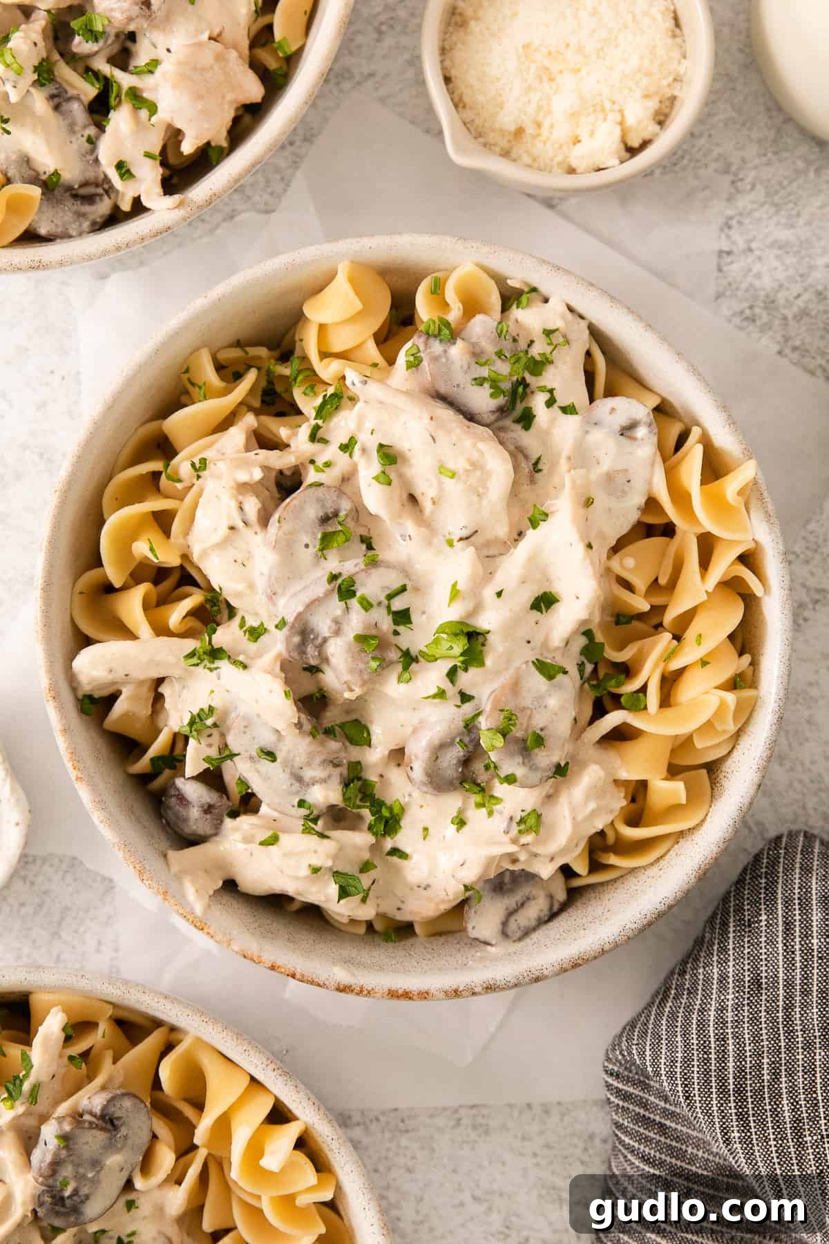 A generous serving of creamy slow cooker cream cheese chicken with mushrooms, perfectly sauced and garnished, presented in a bowl over a bed of pasta.