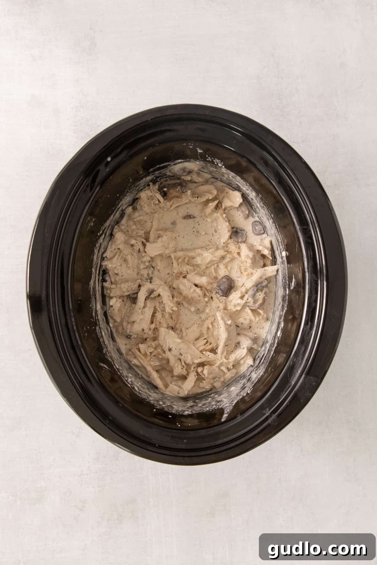 A large black crock pot filled with the finished creamy slow cooker cream cheese chicken and mushrooms, stirred together and ready to be served, showcasing its rich texture.