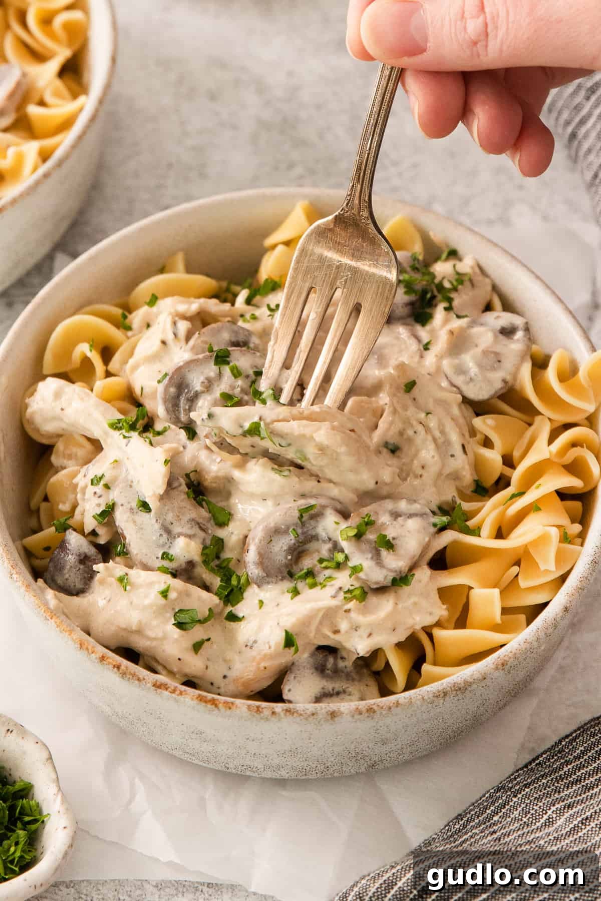 A hand holding a fork, taking a generous bite of creamy slow cooker cream cheese chicken and mushroom risotto, emphasizing the rich, satisfying texture of the dish.