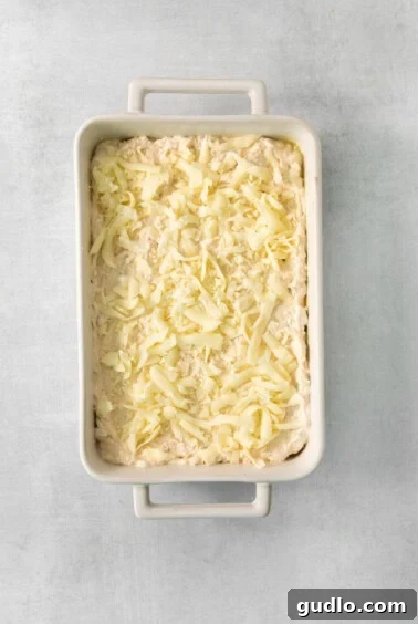 A white baking dish filled with the creamy crab rangoon dip, ready for the final layer of cheese.