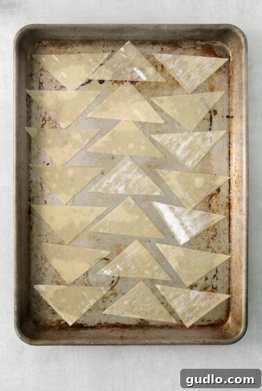 Triangle-shaped wonton wrappers neatly arranged on a baking sheet, prepped for cooking.