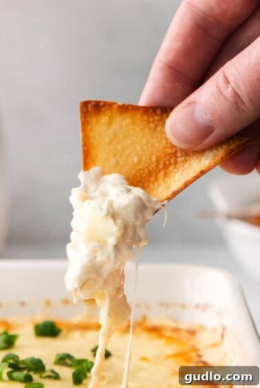 A person dipping a crispy wonton chip into the hot, cheesy crab rangoon dip, fresh from the oven, showcasing the perfect texture for serving.