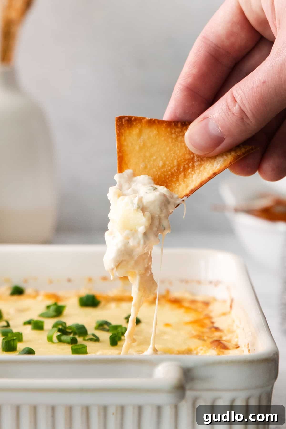 Deconstructed Crab Rangoon Dip 9 A person dipping a perfectly golden wonton chip into a creamy, baked crab rangoon dip, highlighting the rich texture and inviting presentation.