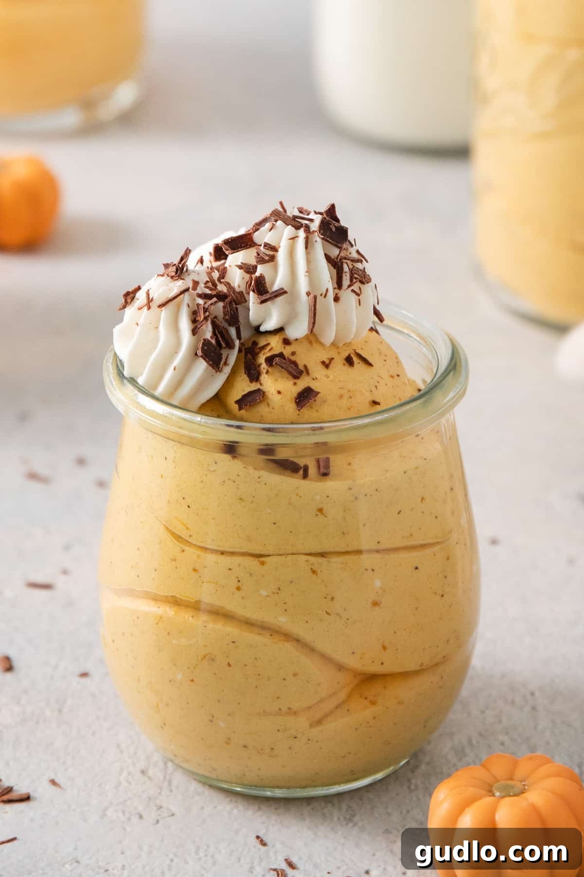 A beautifully presented pumpkin mousse in a glass jar, topped with a generous swirl of whipped cream and a sprinkle of festive spices, ready to be enjoyed.