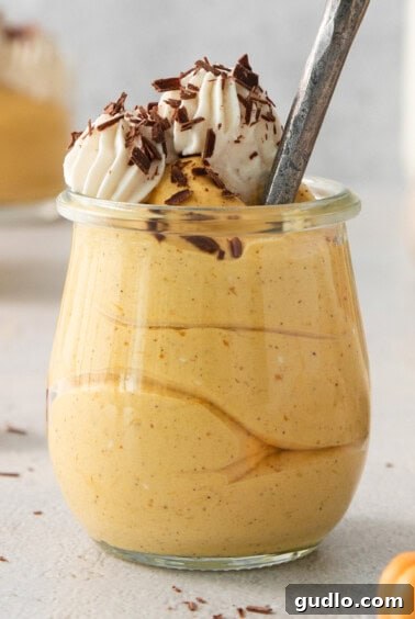 The finished pumpkin mousse dessert in a jar, topped generously with whipped cream and chocolate shavings.