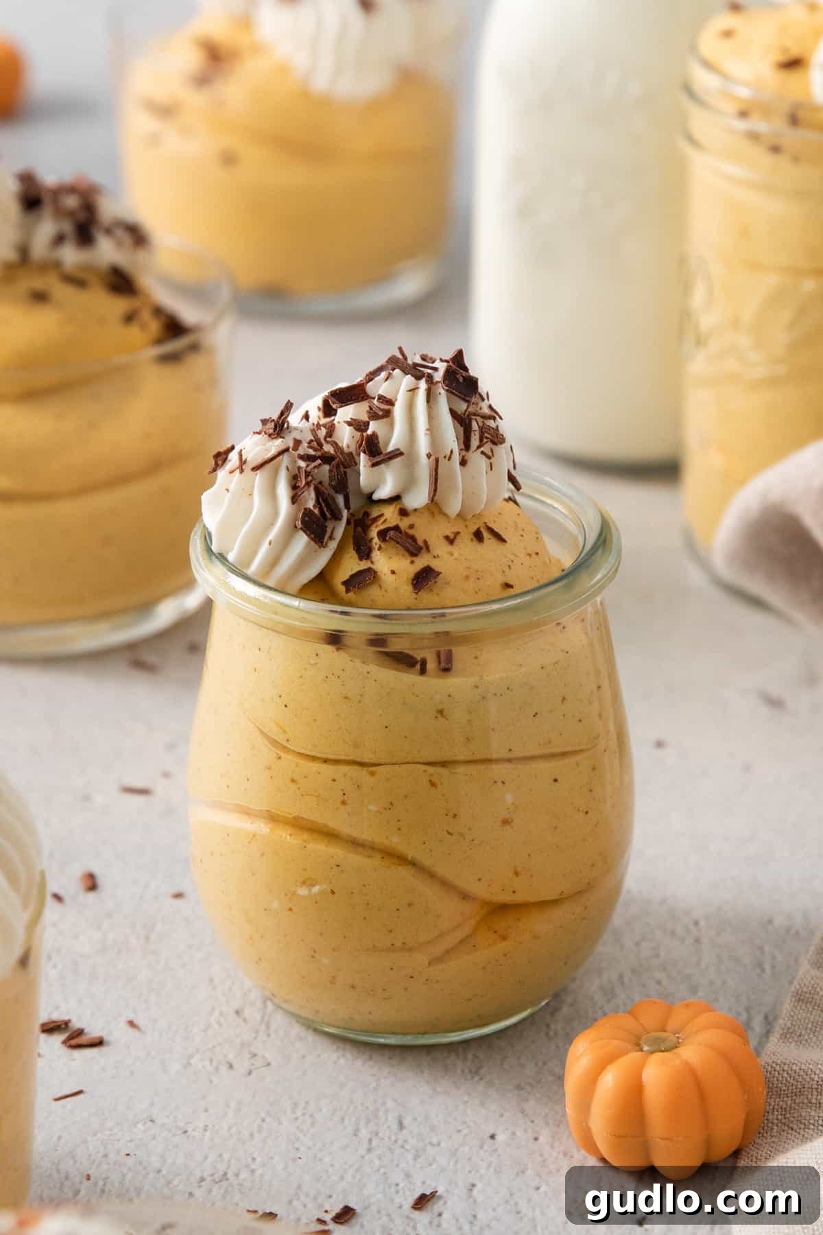A festive pumpkin mousse dessert served in an elegant glass, adorned with a swirl of whipped cream and delicate chocolate shavings, highlighting its rich layers.
