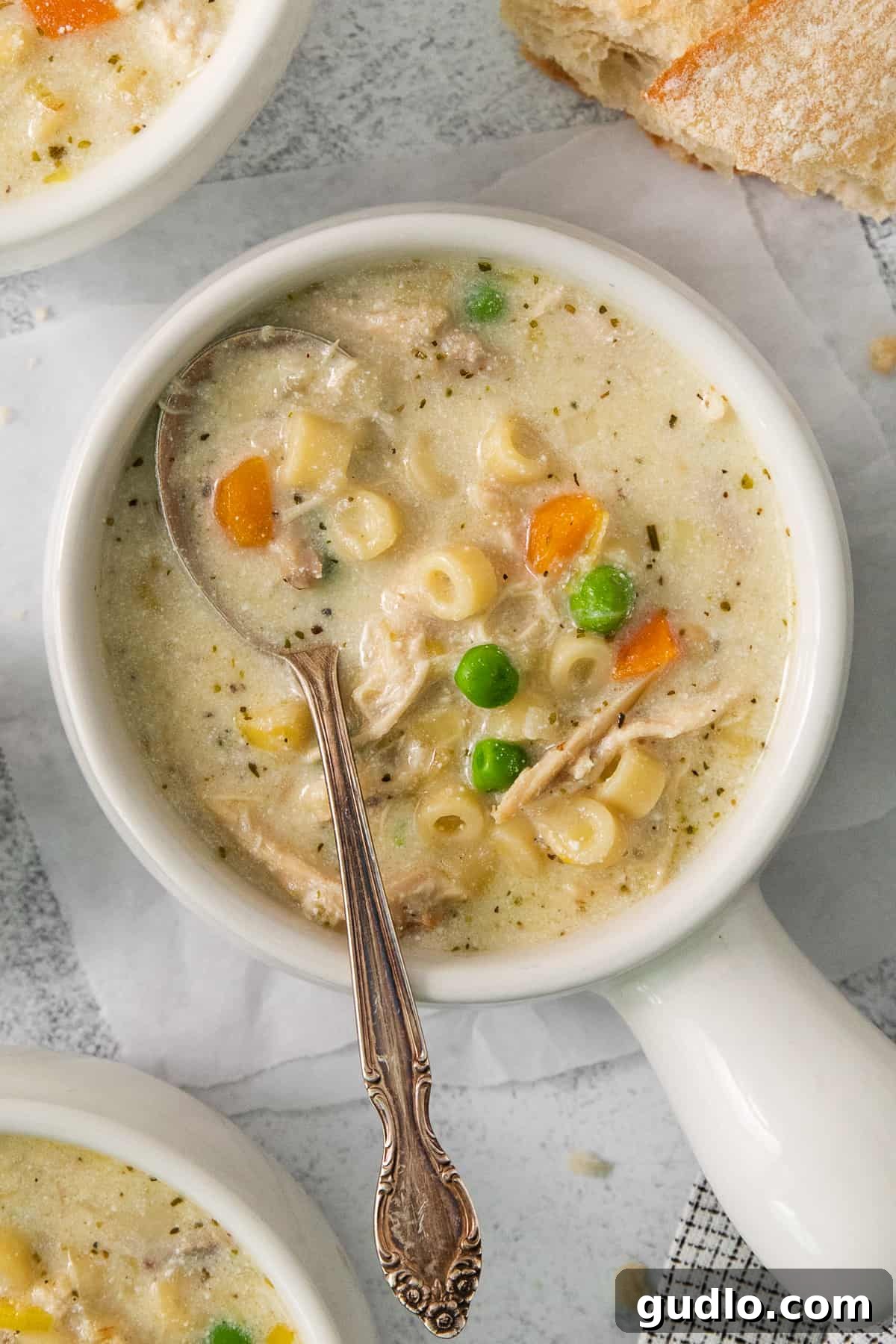 Golden Cream Chicken 2 A beautiful white bowl filled with creamy chicken noodle soup, garnished with fresh herbs and a spoon resting inside, inviting you to take a bite.
