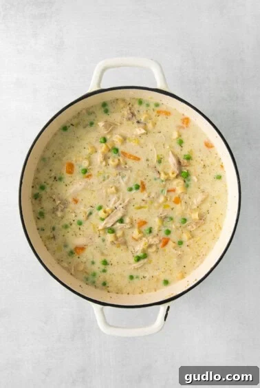 Creamy chicken chowder swirling in a white pot, dotted with green peas and orange carrots, showcasing its rich texture and enticing warmth.