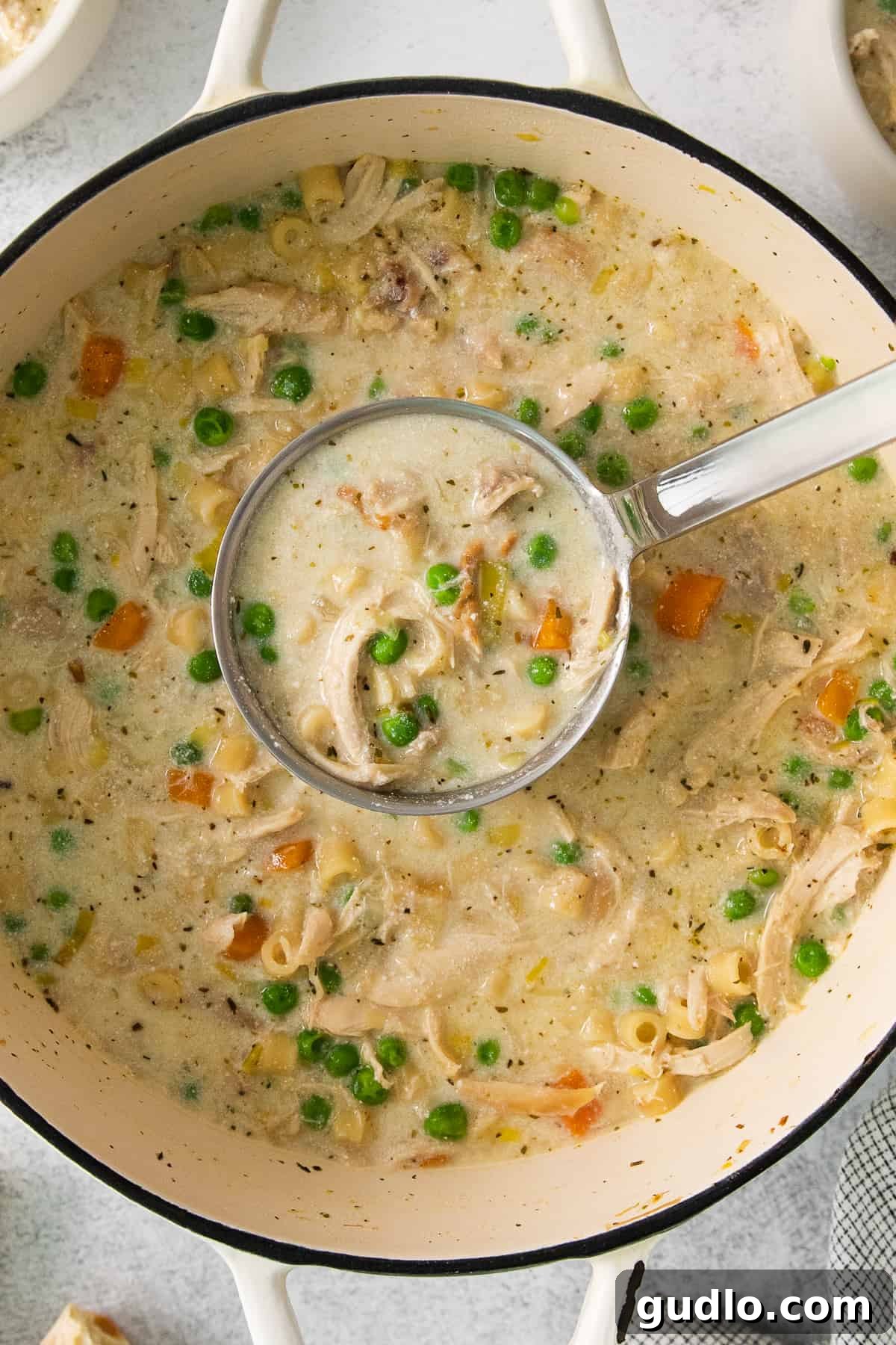 Golden Cream Chicken 7 A close-up of hearty chicken chowder in a white pot, generously filled with tender chicken pieces, vibrant peas, and perfectly cooked carrots, ready to be served.