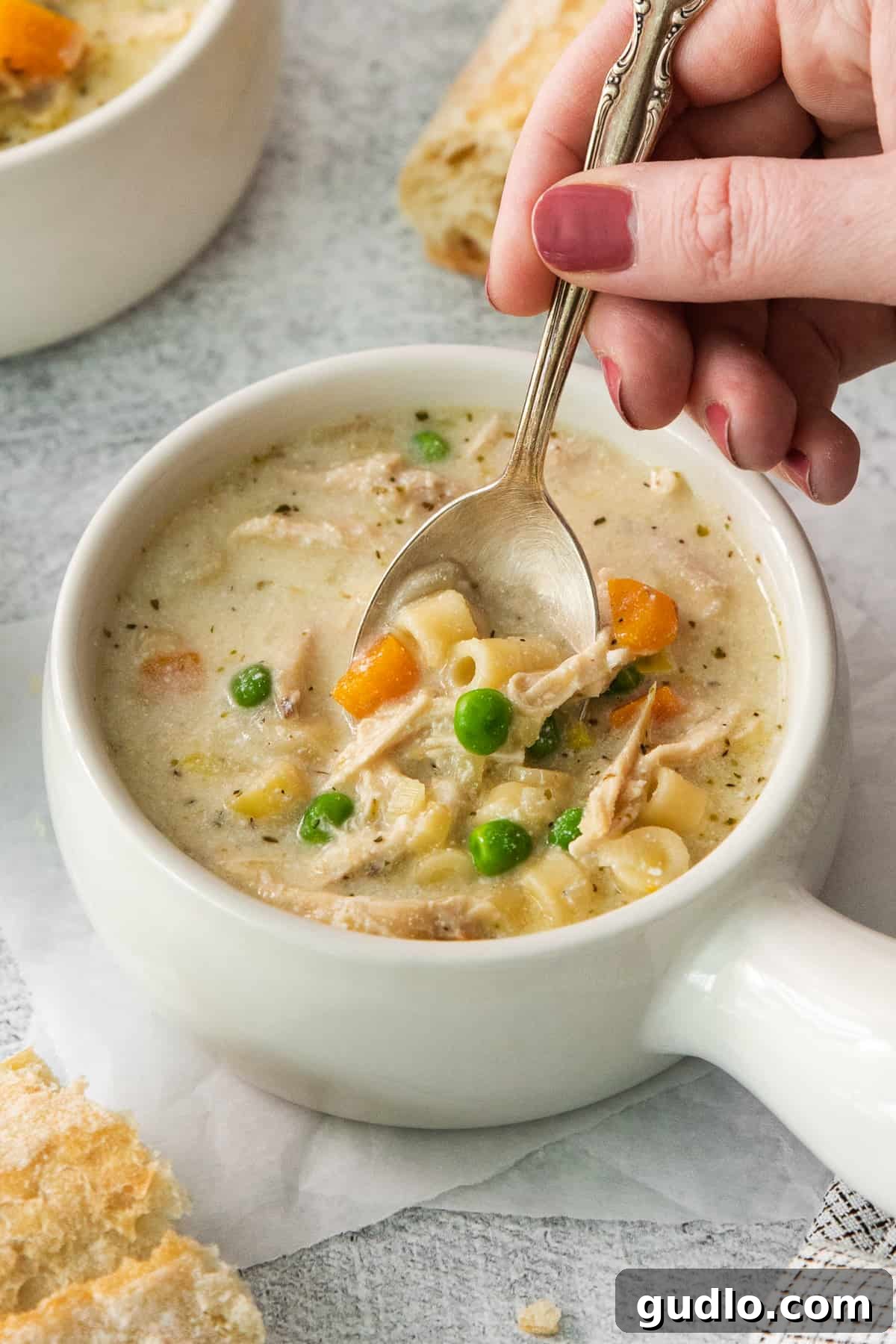Golden Cream Chicken 9 A spoonful of creamy chicken noodle soup being lifted from a white bowl, showcasing the tender chicken, pasta, and vegetables suspended in the rich, creamy broth.