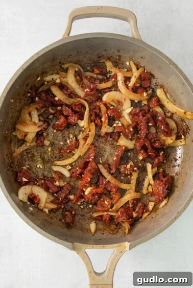 A pan filled with sautéed onions, sun-dried tomatoes, and garlic.