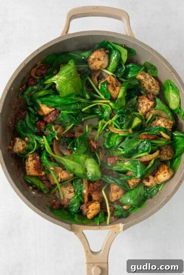 A pan with chicken and fresh spinach wilting into the mixture.