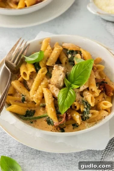 A bowl of pasta with spinach and chicken, garnished with fresh herbs.