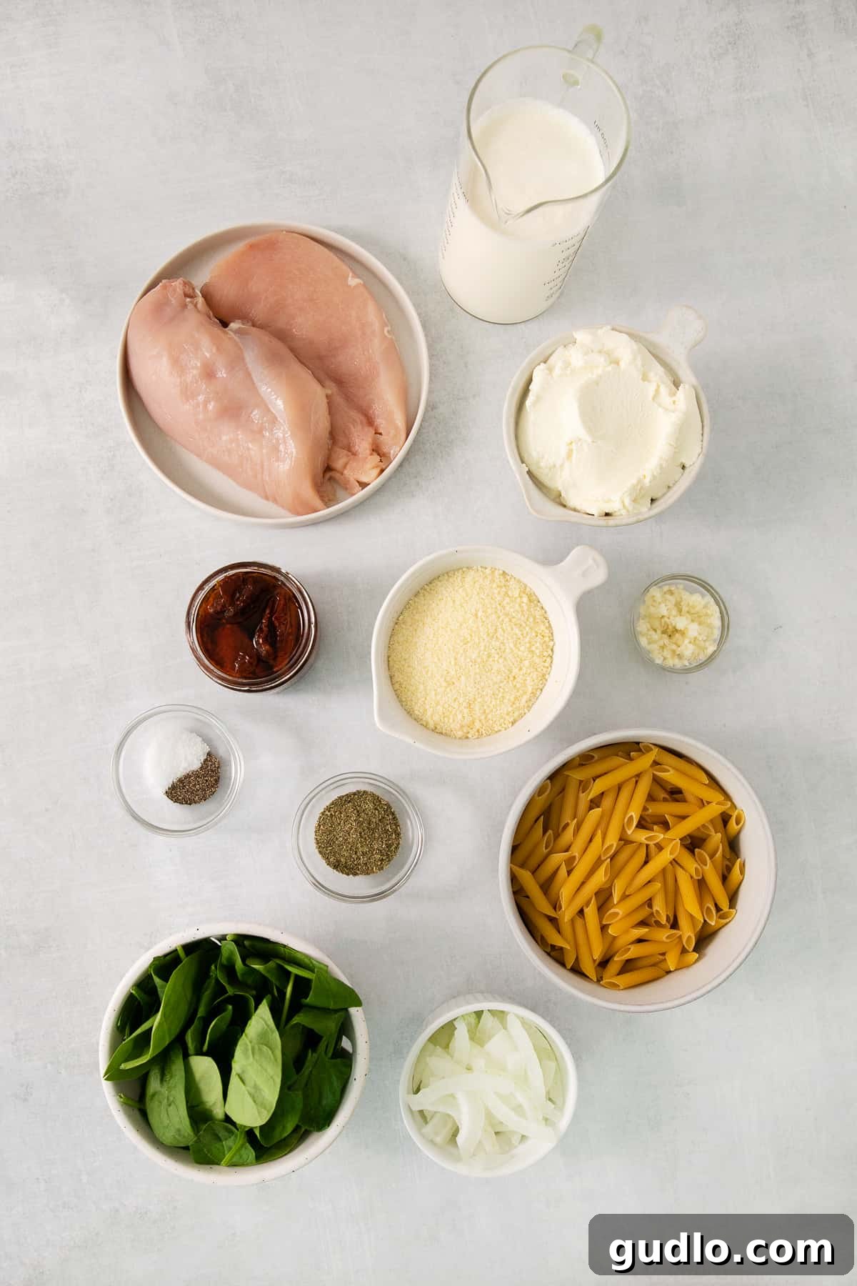 A white table topped with bowls of creamy Tuscan chicken pasta, inviting guests to serve themselves.