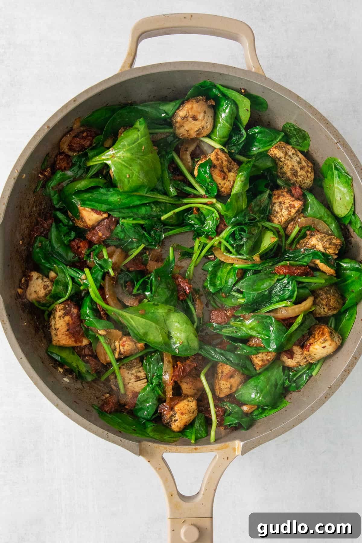 A pan with spinach and chicken in a rich, creamy sauce, simmering gently on the stove.