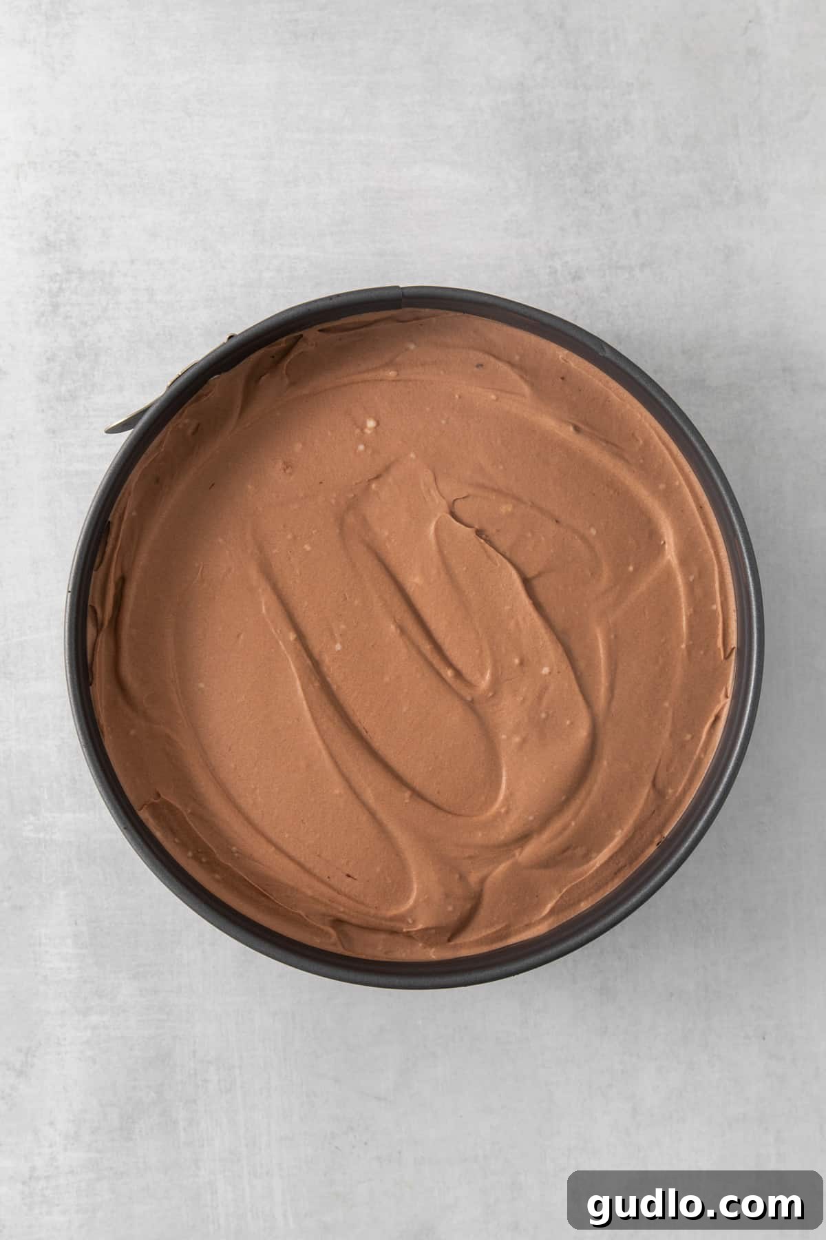 Divine Chocolate Cloud Pie 5 A bowl filled with rich, glossy chocolate frosting sits invitingly on top of a rustic wooden table.