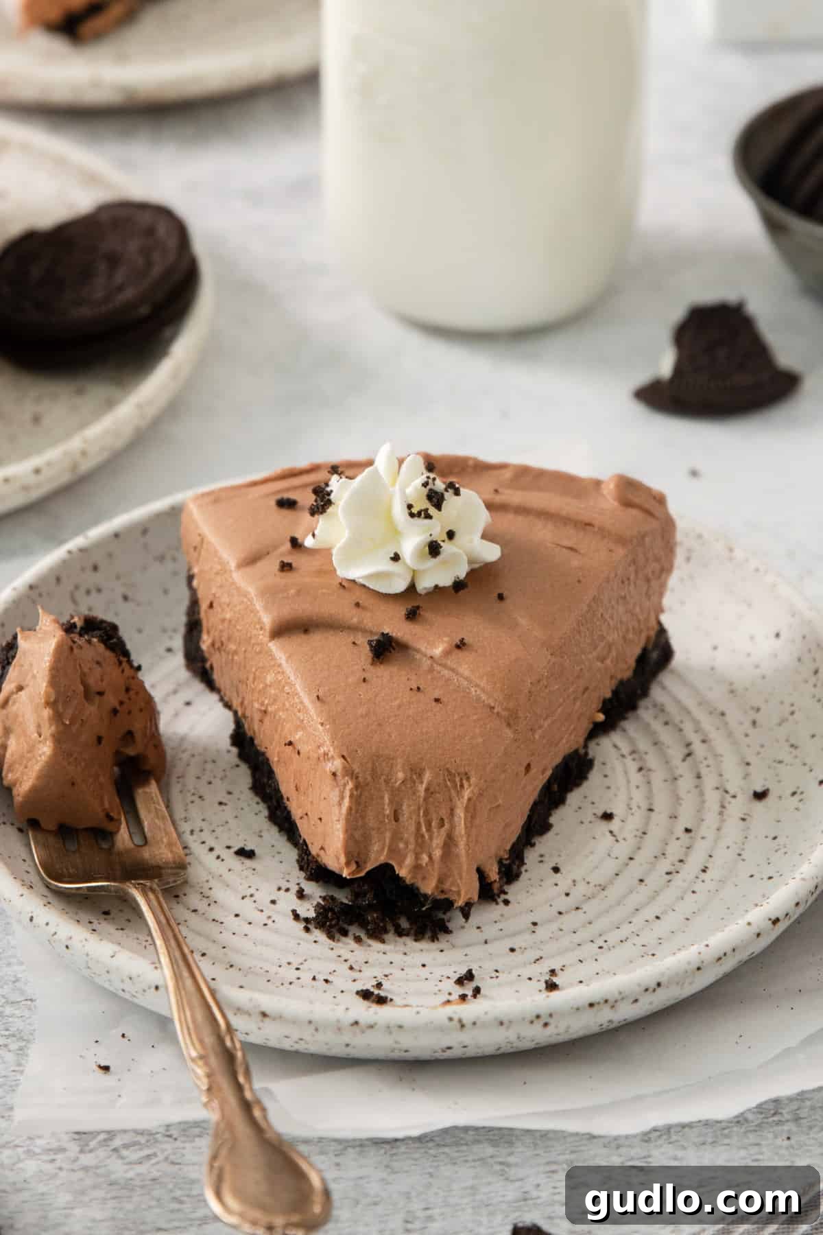 Divine Chocolate Cloud Pie 6 A pristine slice of chocolate mousse pie rests elegantly on a white plate, accompanied by a fork, ready to be enjoyed.