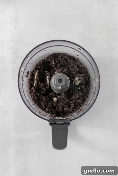 Divine Chocolate Cloud Pie 8 A food processor bowl containing finely crushed Oreo cookies mixed with butter, resembling wet sand.