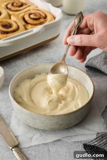 A person uses a spoon to scoop a generous portion of creamy, white homemade icing from a bowl, highlighting its perfect, spreadable consistency.