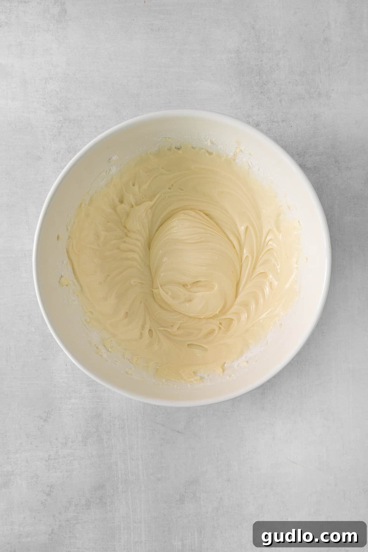 Lush Cream Cheese Frosting for Cinnamon Rolls 6 A pristine white bowl filled with creamy, light-colored frosting, sitting on a wooden cutting board, ready for use.