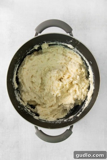 Luxurious Garlic Mashed Potatoes 10 Mashing cooked potatoes with butter, garlic, and ricotta cheese in a pan.